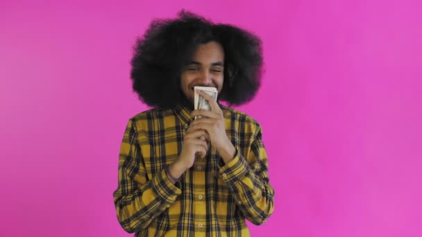 Šťastný Afroameričan drží bankovky v rukou, líbá je a dívá se do kamery, stojí izolovaně na růžovém pozadí — Stock video
