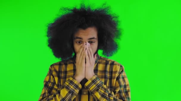 Um jovem com um penteado africano em um fundo verde é surpreendido. Emoções em um fundo colorido. — Vídeo de Stock