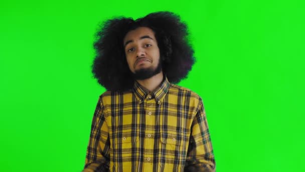 緑の背景にアフリカの髪型の若者が肩をすくめる。色付きの背景の感情. — ストック動画