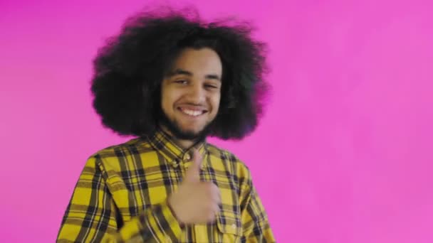 Un uomo afro-americano felice che guarda nella macchina fotografica, mostra un simile con la mano, si trova isolato su uno sfondo rosa — Video Stock