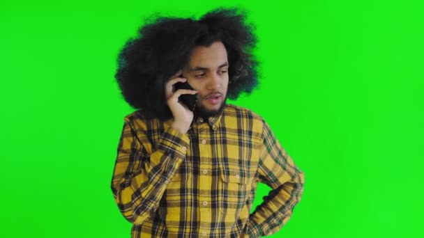 Un giovane con un'acconciatura africana su sfondo verde sta parlando al telefono. Su uno sfondo colorato — Video Stock