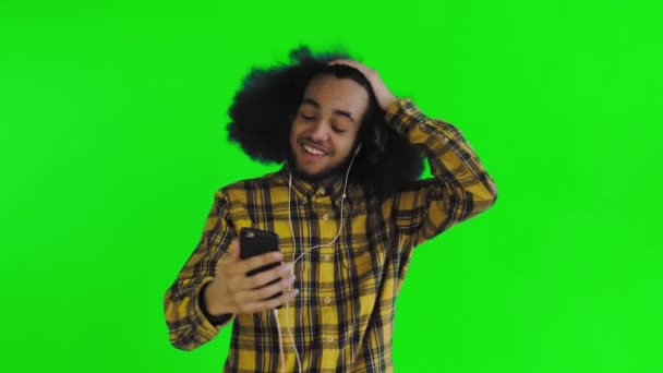 Egy afrikai frizurájú, zöld hátterű, fejhallgatós fiatalember videokapcsolaton keresztül kommunikál. Színes háttérrel — Stock videók