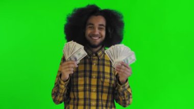 Elinde banknot yelpazesi olan mutlu bir Afro-Amerikalı adam yeşil bir arka planda tek başına kameraya bakıyor.