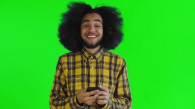 Yeşil arka planda Afrikalı saç stili olan genç bir adam telefona bakar ve mutludur. Renkli bir arkaplanda duygular