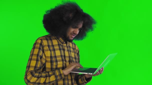 Un jeune homme avec une coiffure africaine sur fond vert tape sur un ordinateur portable. Sur un fond coloré — Video