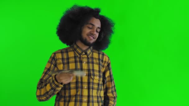 Egy boldog afro-amerikai férfi kezében a bankjegyek rajongóját tartva, és a kamerába nézve, elszigetelten áll a zöld háttéren. — Stock videók