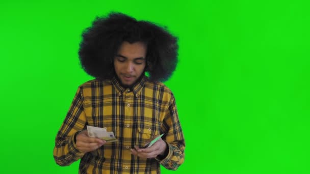 Un uomo afro-americano felice che tiene in mano le banconote, le conta e guarda la macchina fotografica, isolata su uno sfondo verde — Video Stock