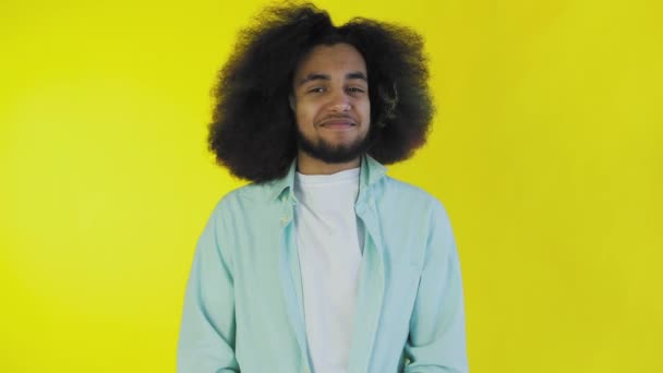 Egy fiatal afroamerikai férfi portréja, egy boldog fickóé, aki sárga háttéren áll és mosolyog a kamerába.. — Stock videók