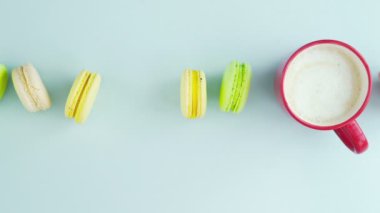 Çok renkli Fransız makarnası kurabiyeleri ve pastel mavi arka planda bir fincan kahve.