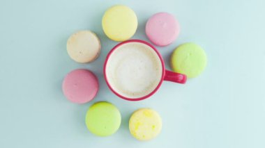 Çok renkli Fransız makarnası kurabiyeleri ve pastel mavi arka planda bir fincan kahve.