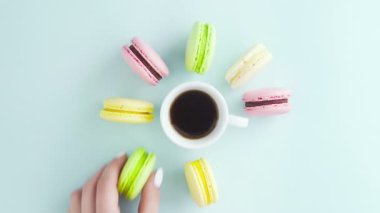 Çok renkli Fransız makarnası kurabiyeleri ve pastel mavi arka planda bir fincan kahve.