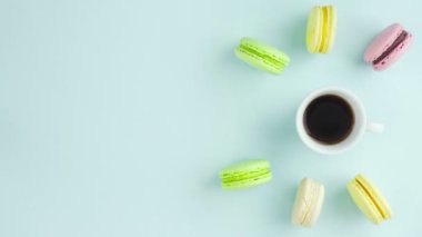 Çok renkli Fransız makarnası kurabiyeleri ve pastel mavi arka planda bir fincan kahve.