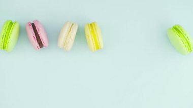 Çok renkli Fransız makarnası kurabiyeleri ve pastel mavi arka planda bir fincan kahve.