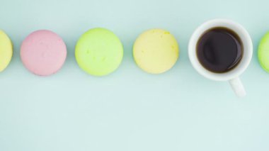 Çok renkli Fransız makarnası kurabiyeleri ve pastel mavi arka planda bir fincan kahve.