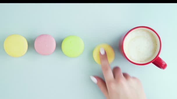 Bovenaanzicht van veelkleurige Franse Macarons koekjes en een kop koffie op een pastelblauwe achtergrond — Stockvideo