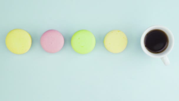 Vista superior de biscoitos Macarons franceses multicoloridos e uma xícara de café em um fundo azul pastel — Vídeo de Stock