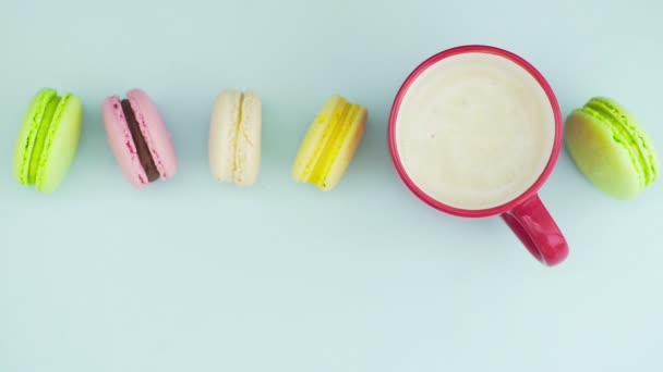 Çok renkli Fransız makarnası kurabiyeleri ve pastel mavi arka planda bir fincan kahve. — Stok video