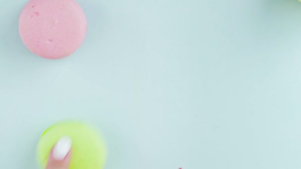 Vista superior de galletas de macarrones franceses multicolores sobre un fondo azul pastel. Una mano de mujer pone galletas — Vídeos de Stock