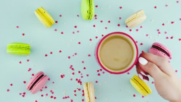 Renkli kurabiyeler, Fransız makarnaları ve pastel mavisi arka planda güzel dağınık konfetiyle bir fincan kahve. — Stok video