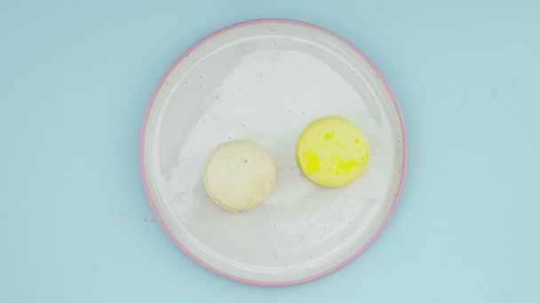Pastel mavi arka planda çok renkli Fransız makarnalı kurabiyelerin üst görüntüsü. Bir kadının eli tabağa kurabiye koyar. — Stok video