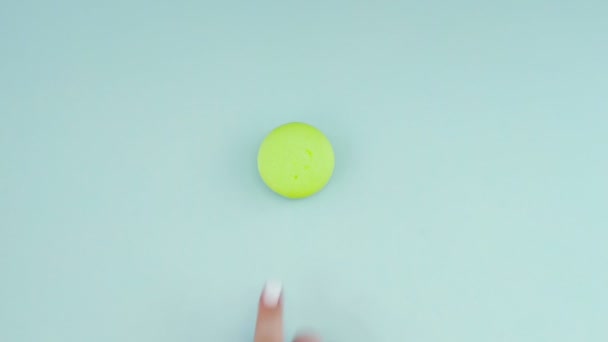 Horní pohled na multi-barevné cookies Francouzské Macarons na pastelově modrém pozadí. Ženská ruka přesune sušenku do středu. — Stock video