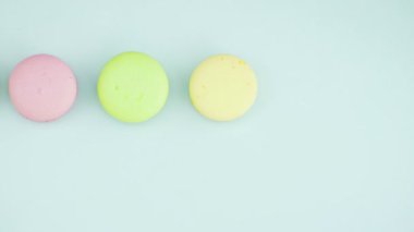 Çok renkli Fransız makarnası kurabiyeleri ve pastel mavi arka planda bir fincan kahve.