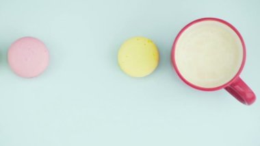 Çok renkli Fransız makarnası kurabiyeleri ve pastel mavi arka planda bir fincan kahve.