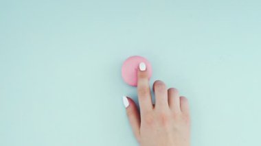 Çok renkli kurabiyelerin üst görüntüsü pastel mavi arka planda Fransız makarnaları. Bir kadının eli kurabiyeyi ortaya taşır..