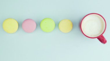 Çok renkli Fransız makarnası kurabiyeleri ve pastel mavi arka planda bir fincan kahve.