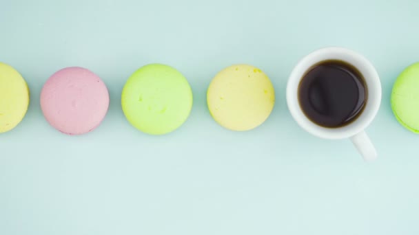 Draufsicht auf bunte französische Macarons-Kekse und eine Tasse Kaffee auf pastellblauem Hintergrund — Stockvideo