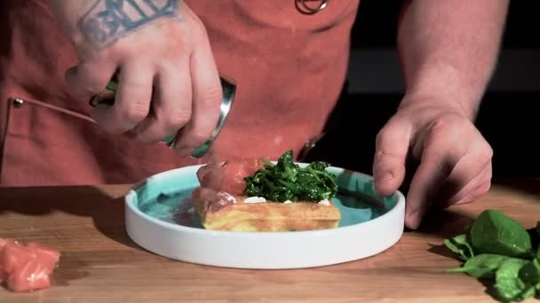 Kuchař sype koření na vafli s červenou rybou a smaženým špenátem v kuchyni. Koncept vaření lahodné jídlo — Stock video