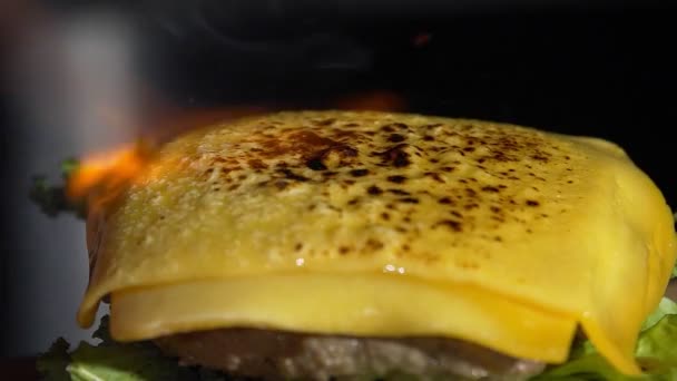 Met behulp van een brander wordt de kaas gesmolten op de hamburger. Close-up van een kok die een hamburger kookt in de keuken. Hamburgers koken met runder- of varkensvlees. — Stockvideo