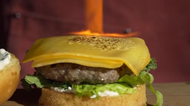 Con l'aiuto di un bruciatore, il formaggio viene fuso sull'hamburger. Primo piano di uno chef che cucina un hamburger in cucina. Hamburger da cucina con cotoletta di manzo o maiale. — Video Stock