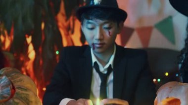 Bir adam mum yakıyor ve ürkütücü kostümlü kızlar Cadılar Bayramı 'nda her iki taraftan mum üflüyor.