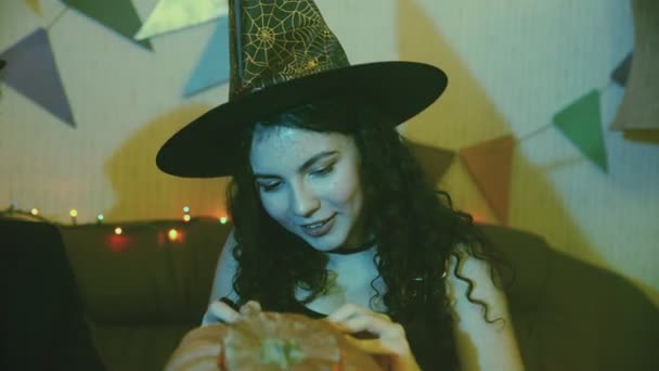 Close-up de uma menina em um traje de Halloween assustador sentado a uma mesa, rindo e esculpir um rosto em uma abóbora — Vídeo de Stock