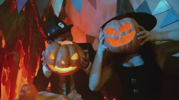 Um cara e uma garota em trajes assustadores com uma pose de Jack-o-lanterna na frente da câmera no Halloween — Vídeo de Stock