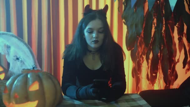 Девушка на вечеринке в честь Хэллоуина, в жутком костюме, просматривает паутину на телефоне — стоковое видео
