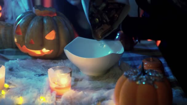 Неузнаваемый человек наливает конфеты в тарелку на Хэллоуин. Жуткая атмосфера. Кошелек или жизнь — стоковое видео