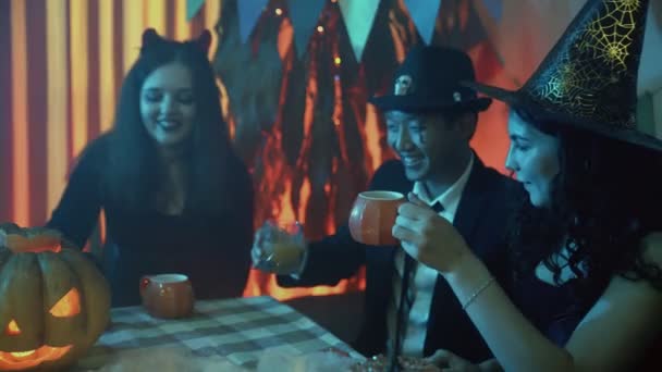 Um grupo de amigos celebra o Halloween e bebe suco à mesa de óculos na forma de uma abóbora — Vídeo de Stock