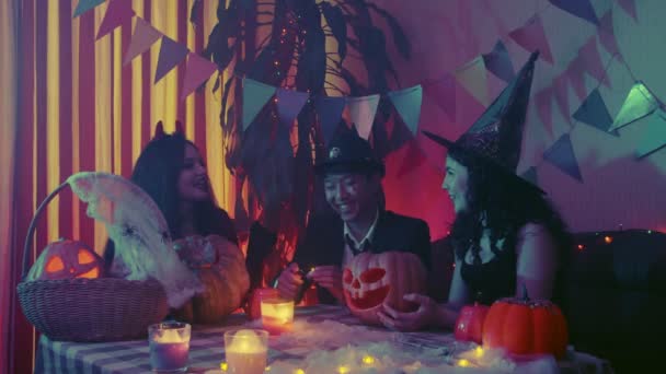 De man stopt een kaars in de pompoen en de pompoen begint te gloeien. Een groep vrienden vieren Halloween door samen te lachen en te chatten. — Stockvideo