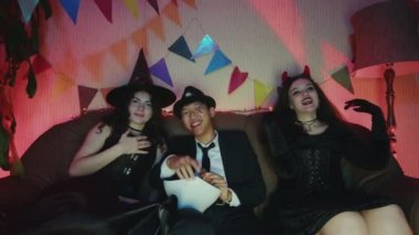Bir grup arkadaş televizyonda Cadılar Bayramı filmi izleyip gülüyor ve sohbet ediyorlar.