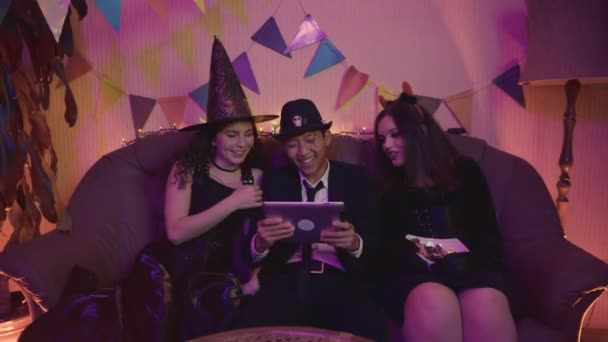 Un grupo de amigos está viendo una espeluznante película de Halloween en una tableta. Riendo y charlando juntos — Vídeos de Stock