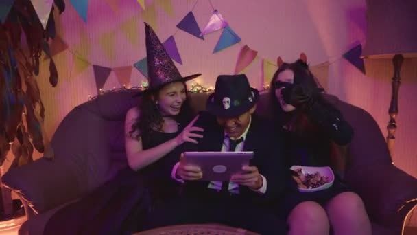 소름끼치는 의상을 입은 남자가 태블릿으로 활발하게 연주하고 있고, 여자들은 즐거운 마음으로 할로윈 파티에서 그를 응원하고 있습니다.. — 비디오