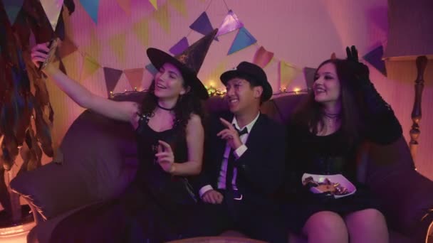 Un groupe d'amis sont assis à une table en costumes effrayants, prendre des photos sur leur téléphone et rire sur Halloween — Video