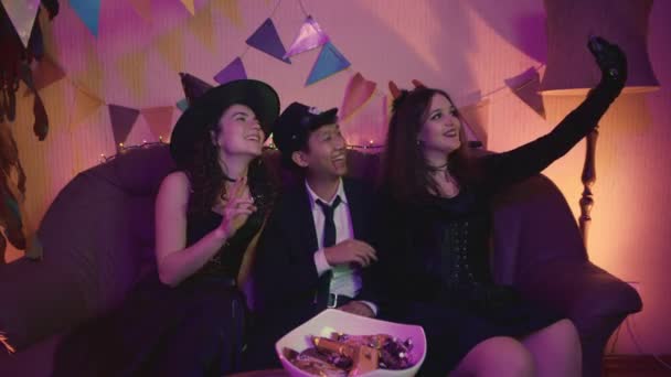 Skupina přátel sedí u stolu ve strašidelných kostýmech, fotí se na telefonu a smějí se na Halloween — Stock video