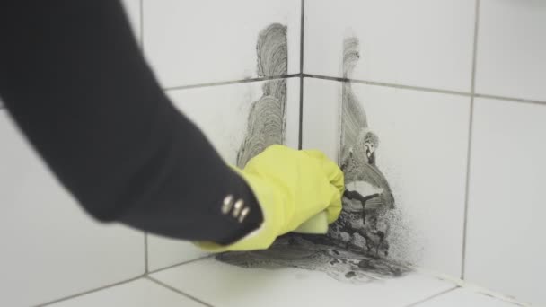 Una mano di donna in un guanto di gomma giallo pulisce lo sporco con una spugna su una piastrella bianca — Video Stock