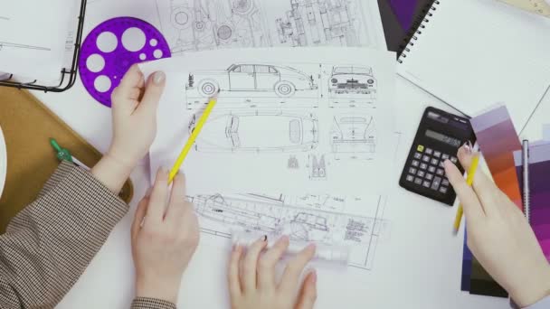 Vue de dessus, deux créatrices à une table discutant de dessins de voitures et comptant sur une calculatrice — Video