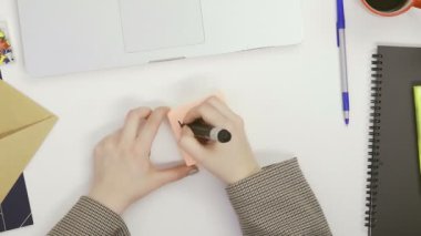 Üst görünümde bir kadın, parlak bir odada bir masada oturan bir kalemle hafıza kartlarına mektuplar yazar.