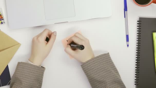 Eine Frau schreibt mit einem Filzstift an einem Tisch in einem hellen Raum Buchstaben auf Memory-Sticker — Stockvideo