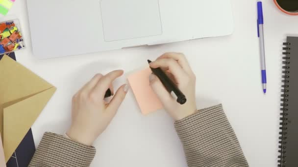 Eine Frau schreibt mit einem Filzstift an einem Tisch in einem hellen Raum Buchstaben auf Memory-Sticker — Stockvideo